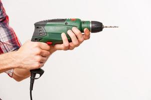 Man using drill. Close-up side view of man using drill while standing against grey background photo