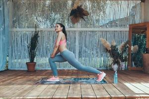 Full length of beautiful young woman in sports clothing doing stretching exercises on patio photo