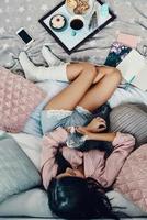 Top view of beautiful young woman in pajamas embracing domestic cat while resting in bed at home photo