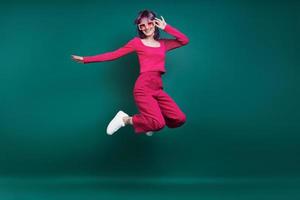 Cheerful young woman jumping against green background photo