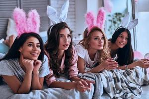 Pure beauties. Four attractive young women in bunny ears smiling and looking away while lying on the bed photo
