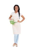 Beautiful gardener. Full length of beautiful young African woman in apron carrying watering can and smiling while standing against white photo