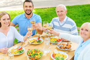 familia brindando con vino. vista superior de la familia feliz sentada en la mesa del comedor y brindando con vino foto