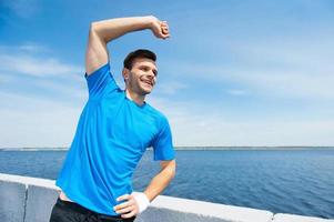 Exercising outdoors. Handsome young man doing stretching exercises while standing outdoors photo