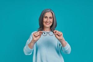 Mature beautiful woman looking at camera and smiling while standing against blue background photo