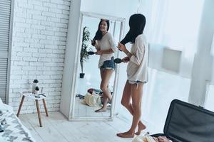 totalmente listo longitud completa de una joven atractiva que combina su cabello y sonríe mientras está de pie cerca del espejo en casa foto