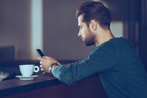 Texting to her. Side view of handsome young man using his smart phone while sitting at bar counter photo