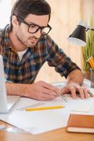 Turning his ideas to reality. Concentrated young man using compass for drawing while sitting at his workplace photo