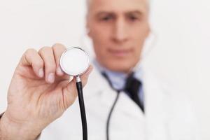 Doctor with stethoscope. Senior doctor in uniform looking at camera and holding his stethoscope outstretched while standing isolated on white photo