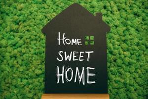 Hogar dulce hogar. primer plano de la pizarra en forma de casa con texto escrito a mano en el fondo de musgo foto