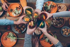 Cheers Top view of people cheering with drinks while sitting at the rustic dining table photo