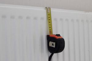 Yellow tape measure centimeters with metal clip hanging on radiator, horizontal photo. Construction and repair tool, measuring length instrument, closeup photo