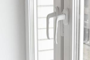 White plastic window handles detail, closeup view, horizontal photo. Closed modern windows in flat, PVC plastic, handles turned down side view, cold weather photo