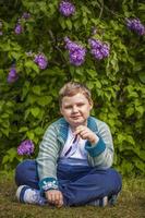 un niño posa cerca de una exuberante lila. retrato de niños con una interesante expresión facial. interacciones. enfoque selectivo. foto