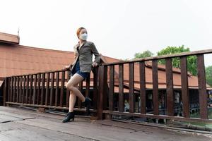 Young asian woman traveler with mask and backpack posting on the bridge in the morning photo