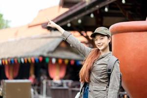 Young asian woman traveler with mask and backpack pointing finger on famous tourist attractions in thailand. Emotion smile photo