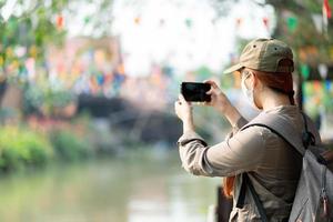 joven viajero asiático con sombrero, mochila y máscara tomando fotos mientras viaja solo en ayutthaya tailandia