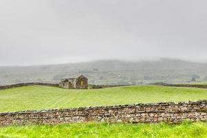 muro de piedra con antiguo granero de piedra en la niebla foto