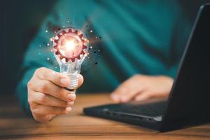 Man holding a light bulb while working on the computer to think and create new ideas with technological innovations and creativity Ideas inspired by online technology, innovations. photo