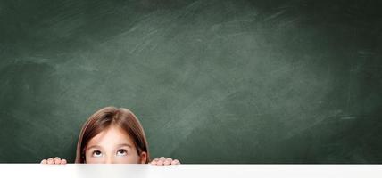 linda niña pequeña mirando hacia arriba en el escritorio de la escuela. foto