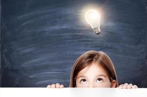 Young cute girl at chalkboard with light bulb over head photo