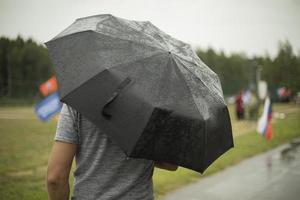 Black umbrella in rain. Large umbrella in bad weather. Man on street on cloudy day. photo