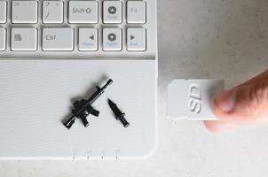 la mano inserta una tarjeta SD compacta en la ranura de la netbook, en la que se encuentran un cuchillo en miniatura y una pistola. el concepto de juegos de computadora sobre temas militares, tiradores en línea y simuladores de guerra foto