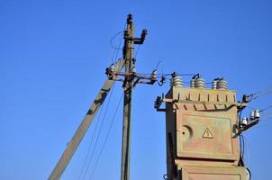 Old and obsolete electrical transformer against the background of a cloudless blue sky. Device for distribution of supply of high-voltage energy photo