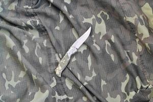 Military knife on army camouflage clothes close up. Background with copy space for military or special service design photo