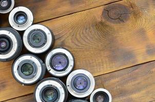 Several photographic lenses lie on a brown wooden background. Space for text photo