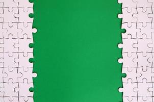 Fragment of a folded white jigsaw puzzle on the background of a green plastic surface. Texture photo with copy space for text