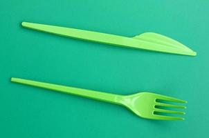 Disposable plastic cutlery green. Plastic fork and knife lie on a green background surface photo