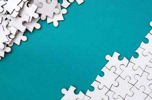Fragment of a folded white jigsaw puzzle and a pile of uncombed puzzle elements against the background of a blue surface. Texture photo with space for text