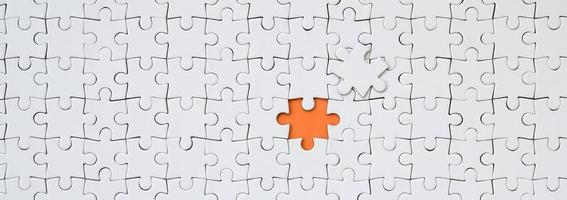 The texture of a white jigsaw puzzle in an assembled state with one missing element forming an orange space photo