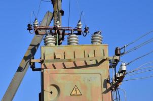 Old and obsolete electrical transformer against the background of a cloudless blue sky. Device for distribution of supply of high-voltage energy photo