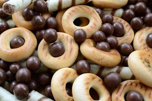 A lot of crispy sweet tubules, chocolate melting balls and yellow bagels lie on a wooden surface. Close up view photo