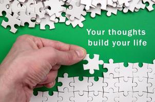 Your thoughts build your life. The hand folds a white jigsaw puzzle and a pile of uncombed puzzle pieces lies against the background of the green surface photo