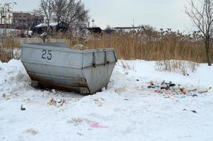 Trash bin at the side of street in winter with lip garbage container winter snow. Metal container for household waste photo