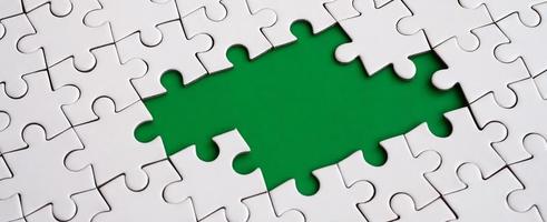 Close-up texture of a white jigsaw puzzle in assembled state with missing elements forming a green pad for text. Copy space photo
