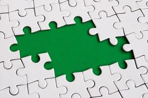 Close-up texture of a white jigsaw puzzle in assembled state with missing elements forming a green pad for text. Copy space photo