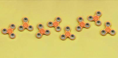 Many orange fidget spinners lies on texture background of fashion pastel orange color paper photo