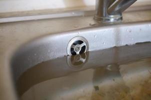 Stainless steel sink plug hole close up full of water and particles of food photo