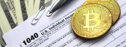 The pen, bitcoins and dollar bills is lies on the tax form 1040 U.S. Individual Income Tax Return. The time to pay taxes photo