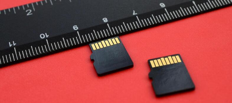 Two small micro SD memory cards lie on a red background next to a black ruler. A small and compact data and information store photo