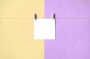 A piece of paper is hanging on a rope with pegs on texture background of fashion pastel yellow and violet colors photo