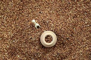 Background image of a large pile of buckwheat, in the middle of which lies a small jug and a wooden spatula for cereals photo