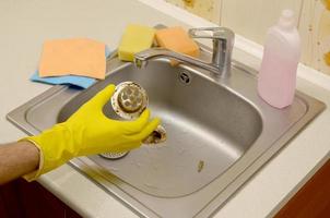 Cleaner in rubber gloves shows waste in the plughole protector of a kitchen sink photo