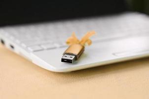 Orange usb flash memory card with a bow lies on a blanket of soft and furry light orange fleece fabric beside to a white laptop. Classic female gift design for a memory card photo