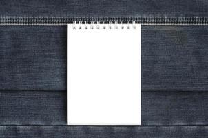 White notebook with clean pages lying on dark blue jeans background. Image with copy space photo