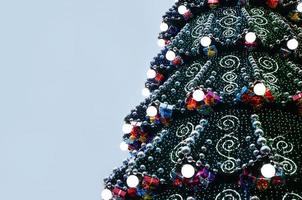 A fragment of a huge Christmas tree with many ornaments, gift boxes and luminous lamps. Photo of a decorated Christmas tree close-up with copy space